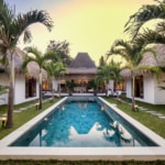 The pool area is surrounded by palm trees and garden at Cocotier Seminyak villa walking distance to Seminyak beach