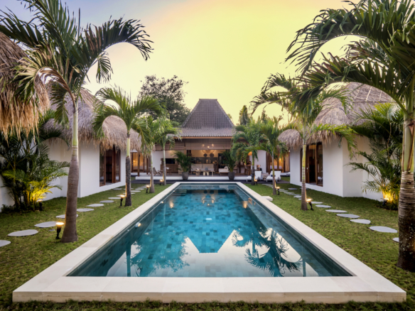 The pool area is surrounded by palm trees and garden at Cocotier Seminyak villa walking distance to Seminyak beach