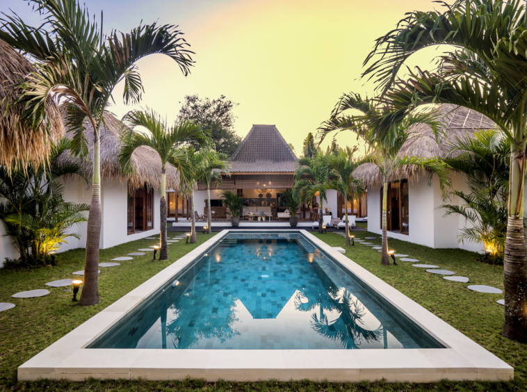 The pool area is surrounded by palm trees and garden at Cocotier Seminyak villa walking distance to Seminyak beach