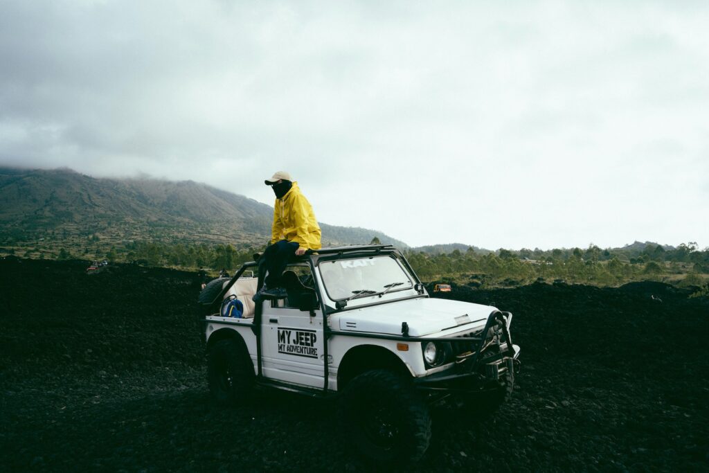 A guy with a yellow jacket sitting on top of a white jeep on a cloudy day while doing the Mount Batur hike